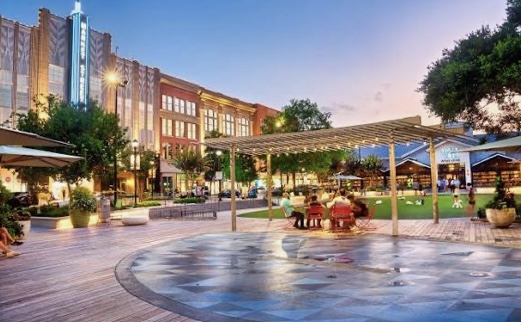 Town Green Park in The Woodlands, Texas at sunset with families gathered near shops and restaurants, a popular area for real estate and community living