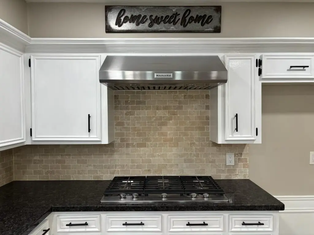 Modern farmhouse kitchen with white cabinets, stainless steel vent hood, and tile backsplash in a Spring, TX home for sale