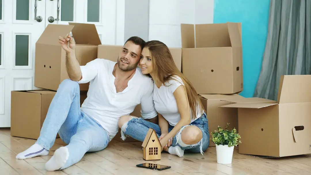 Couple sitting on the floor surrounded by moving boxes after buying their new home in Spring, Texas