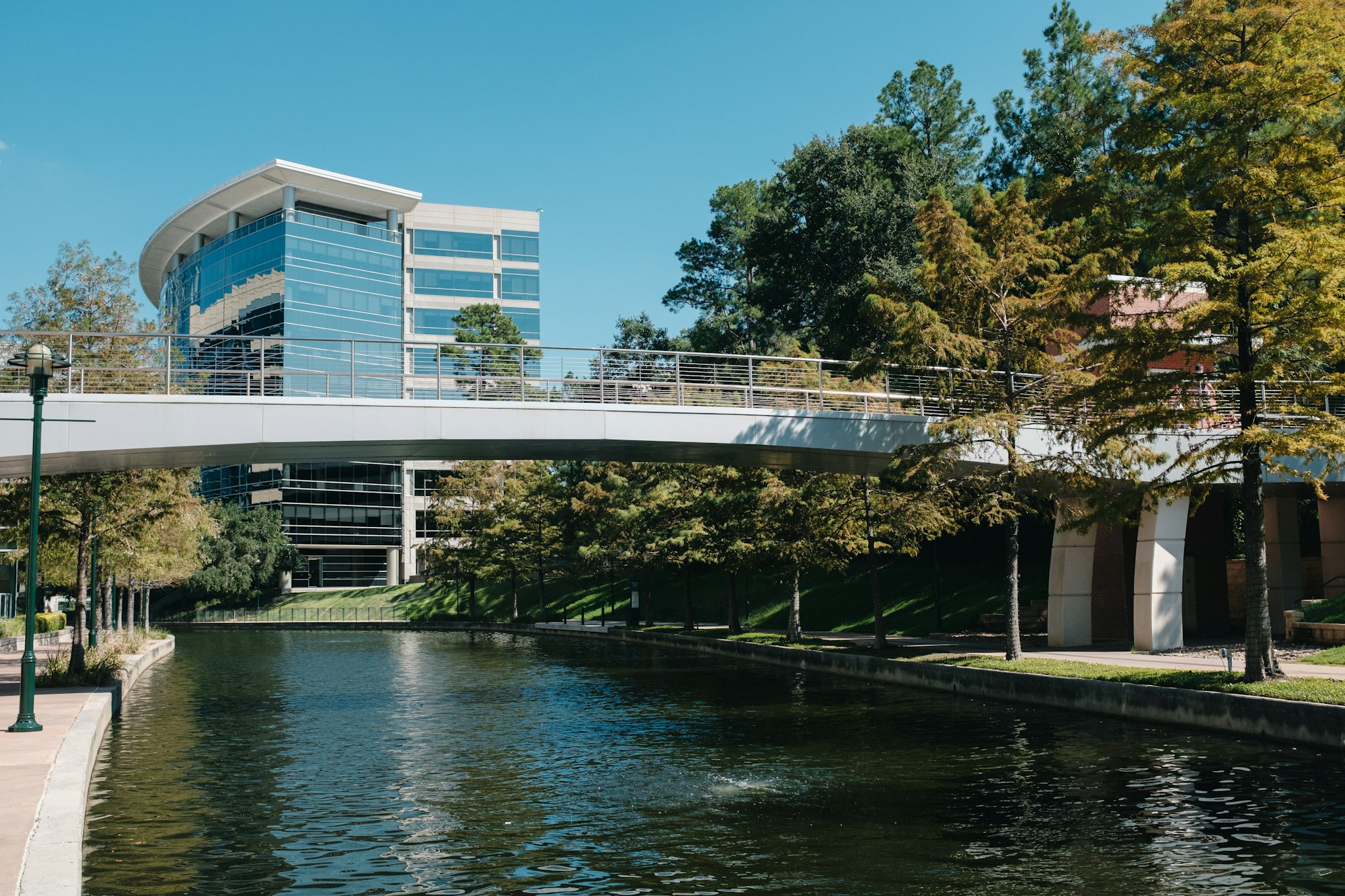 The Woodlands Waterway footbridge with office towers and trees along the water in The Woodlands, Texas